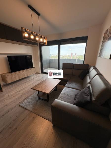 Obývačka s pohovkou, podlahou s dreveným dekorom a veľkým oknom v 2-izbovom byte.