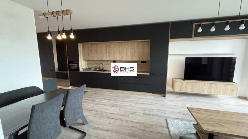 Obývacia izba v 2-izbovom byte so sivá kuchyňou a televíziou, podlaha s dreveným dekorom.