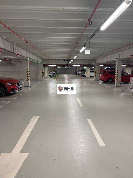 Podzemná garáž so zaparkovanými autami a osvetlením v 2-izbovom byte.